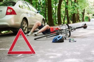 A cyclist riding on a city street, wearing a helmet and looking concerned after being hit by a car.