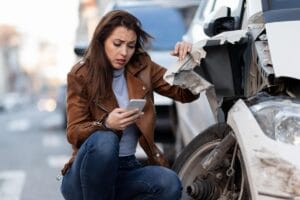 Worried driver on her phone beside a car with heavy front-end damage after another vehicle pulled out, illustrating fault in an Illinois failure-to-yield accident