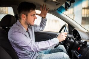 Young driver looking alarmed with a hand raised behind the wheel, illustrating the risks of being hit by an unlicensed driver in Illinois