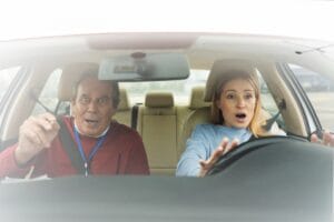 Front-seat passenger reaches for the steering wheel as another person drives, illustrating car owner liability when someone else drives your car in Illinois